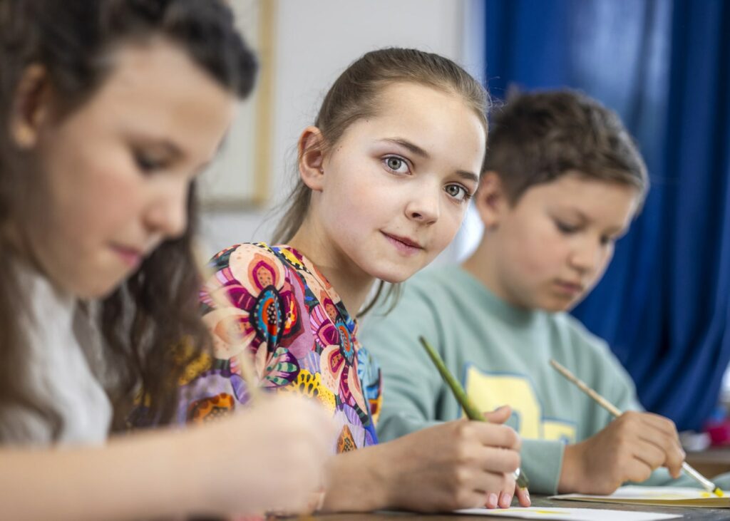 Foto zweier Schülerinnen und ein Schüler im Kunstunterricht der SABEL Schule. Die Schülerin Inder Mitte schaut direkt in die Kamera. Sinnbild für den angedachten Unterricht auf dem Bildungscampus Taufkirchen.