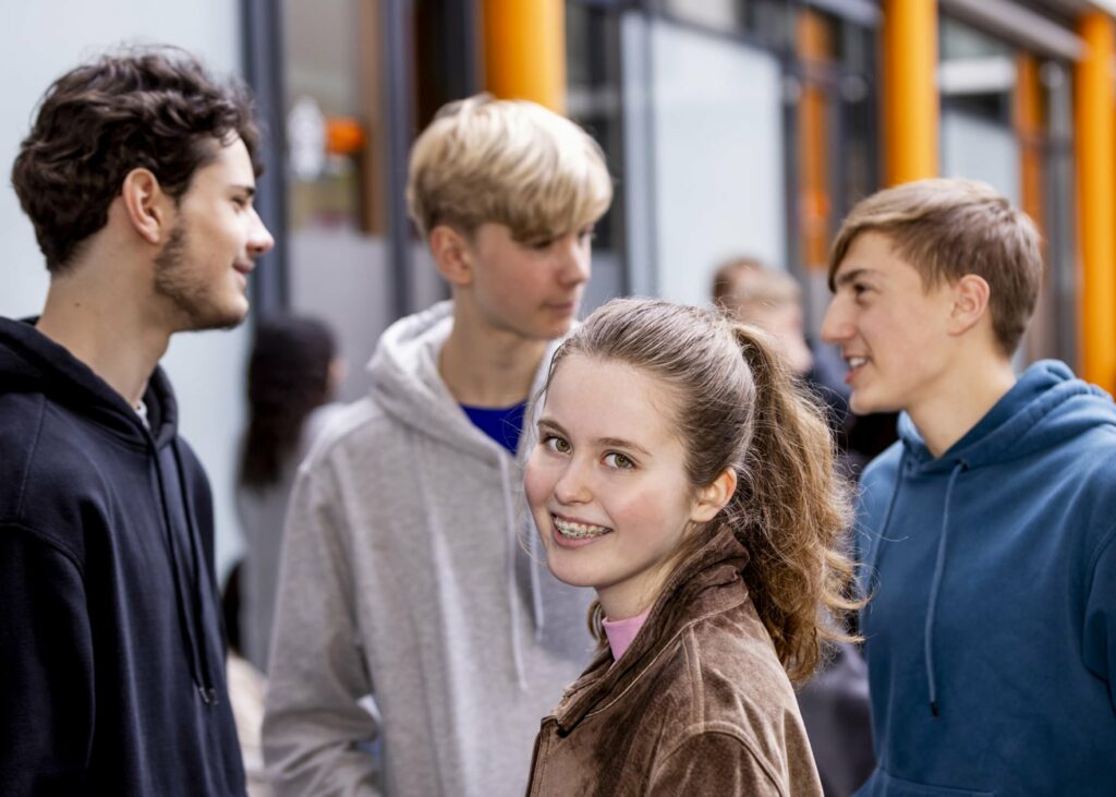 Foto einer Schülerin und dreier Schüler, die in einer Gruppe stehen und an der SABEL Schule die Pause verbringen. Sinnbild für den angedachten Bildungscampus Taufkirchen.